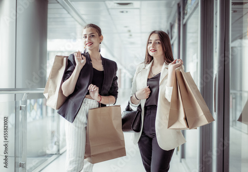 Two beautiful young caucasian happy shopaholic women with shopping bags walk in shopping mall.