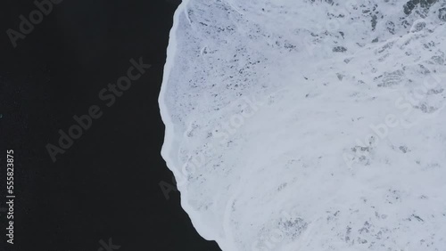 Aerial top view shot of foamy waves of ocean reaching black sand beach in Iceland photo