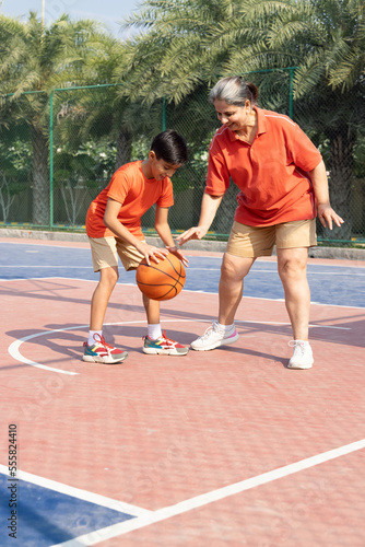 Grandmother and grandson having fun playing with basketball at basketball court.