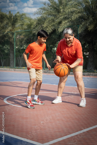 Grandmother and grandson having fun playing with basketball at basketball court.