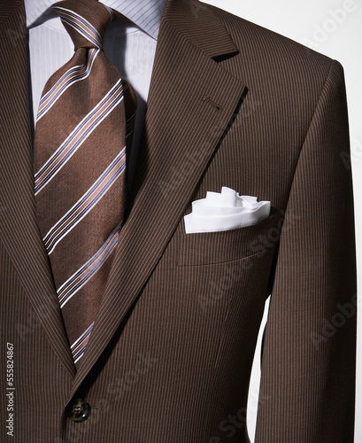 Detail of a bown suit jacket with shirt, white handkerchief and brown striped necktie
