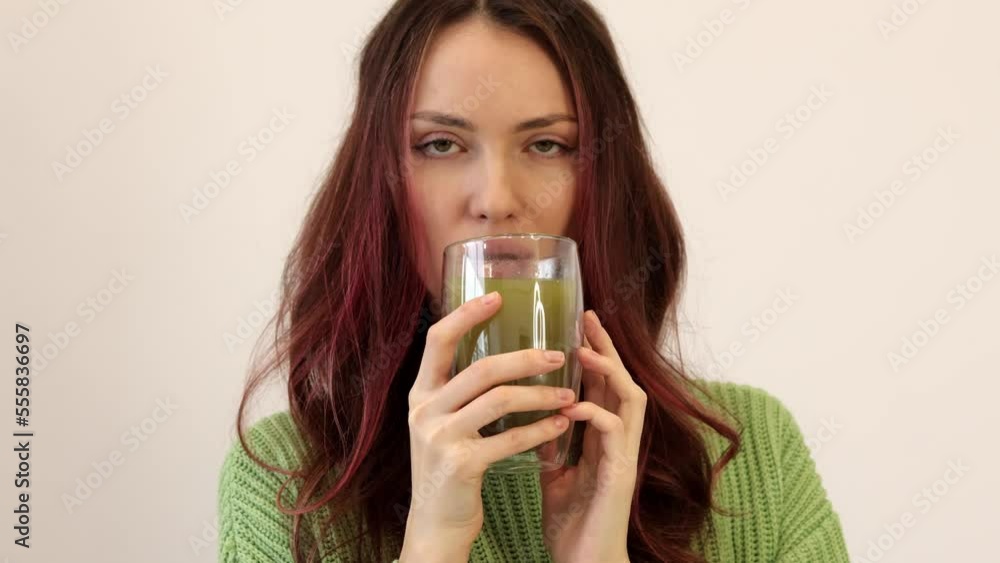 Smiling woman in a good mood drinking matcha A beautiful girl in a green sweater holds a cup of hot matcha tea in her hand in a clear glass. Smiling woman in a good mood drinking matcha A beautiful girl in a green sweater holds a cup of hot matcha tea in her hand in a clear glass.
