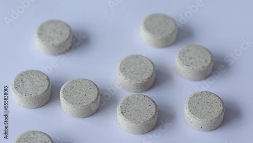 Supplements with chewable tablets DGL liquorice root. Round puck tablets of beige color with dark droplets on a white background view from above.