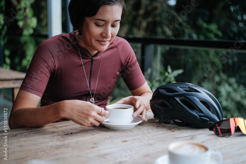 A young female cyclist having a cup of coffee at a cafe by the mountains.