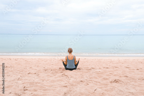 The girl is sitting in the lotus position and meditating on the sand on the beach