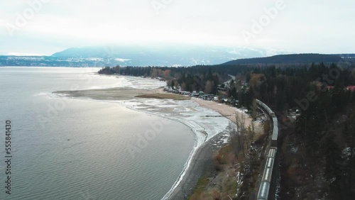 During the winter months near Salmon Arm, British Columbia, Canada, there is a train traveling along the tracks on a railroad next to Shuswap Lake, in a Cinematic Reverse Reveal shot.Canada. photo