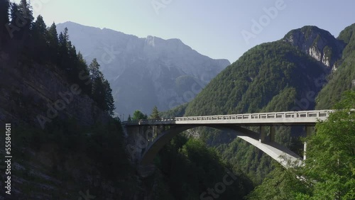 Push in wide drone shot of tall modern arch bridge surrounded by mountain peaks - huge rocky mountain range in the background. Slovenia, Alps, Europe photo