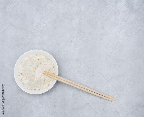 Cooked white rice in white bowl with wood sticks on grey background. Selective focus. Asian food concept