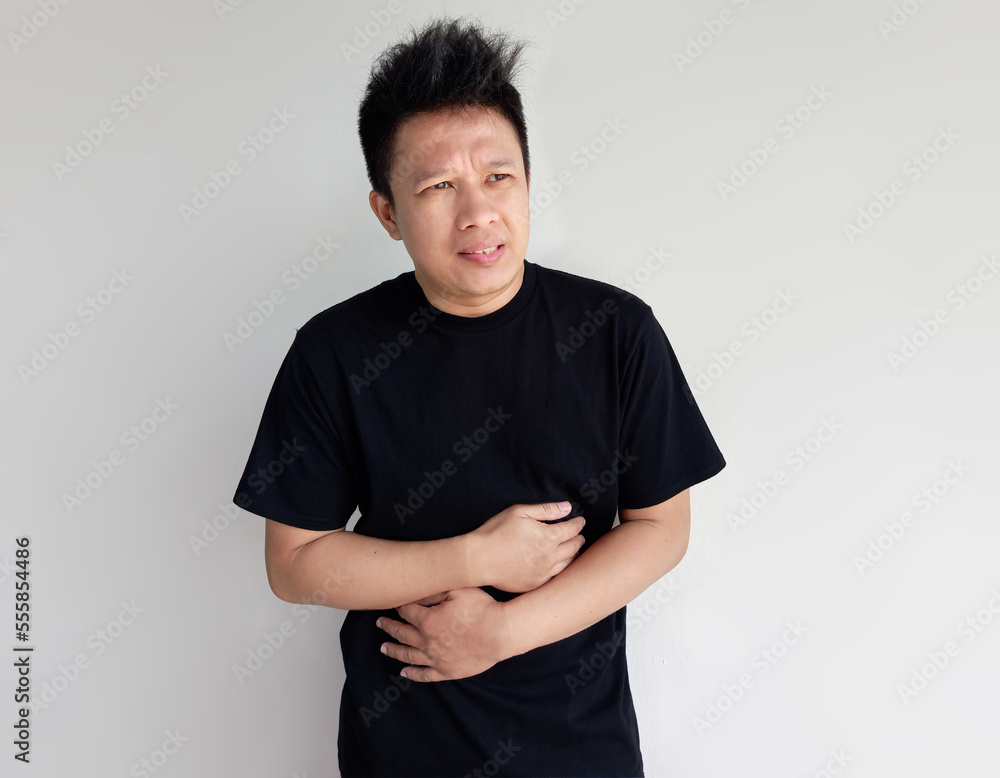 Obraz premium Young man has stomach ache with hand holding stomach isolated on plain background