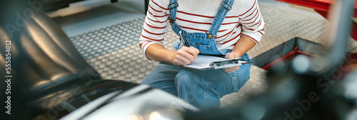 Unrecognizable mechanic woman with clipboard checking motorcycle and taking notes on factory