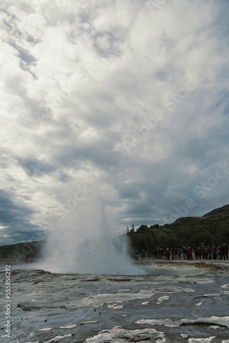 Tourist group at Strokkur geyser landscape photo. Beautiful nature scenery photography with grey sky on background. Idyllic scene. High quality picture for wallpaper, travel blog, magazine, article
