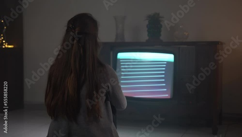 Woman wasting time watching retro TV with bad cable signal, female sitting on the floor and starring vintage TV screen with blinking stripes and noise interference. Grain and distortion on retro TV