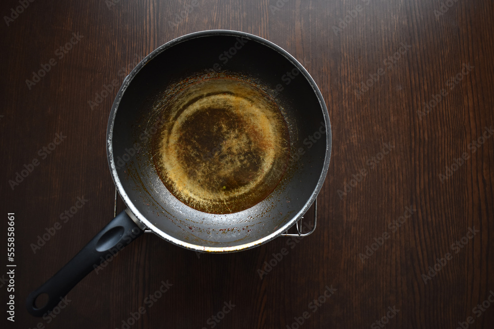 Dirty old scratched non-stick pan or wok on wood table. Teflon pan peeling off. Copy space is on the right side. Dirty old scratched non-stick pan or wok on wood table. Teflon pan peeling off. Copy space is on the right side.