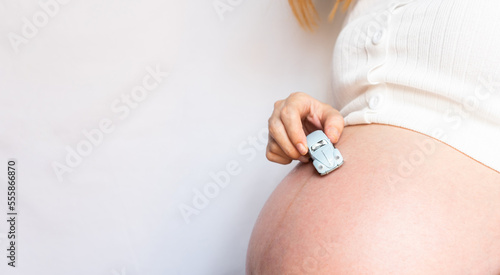 Pregnant woman in white shirth hand holding children’s car toy on tummy The concept of happy motherhood. photo