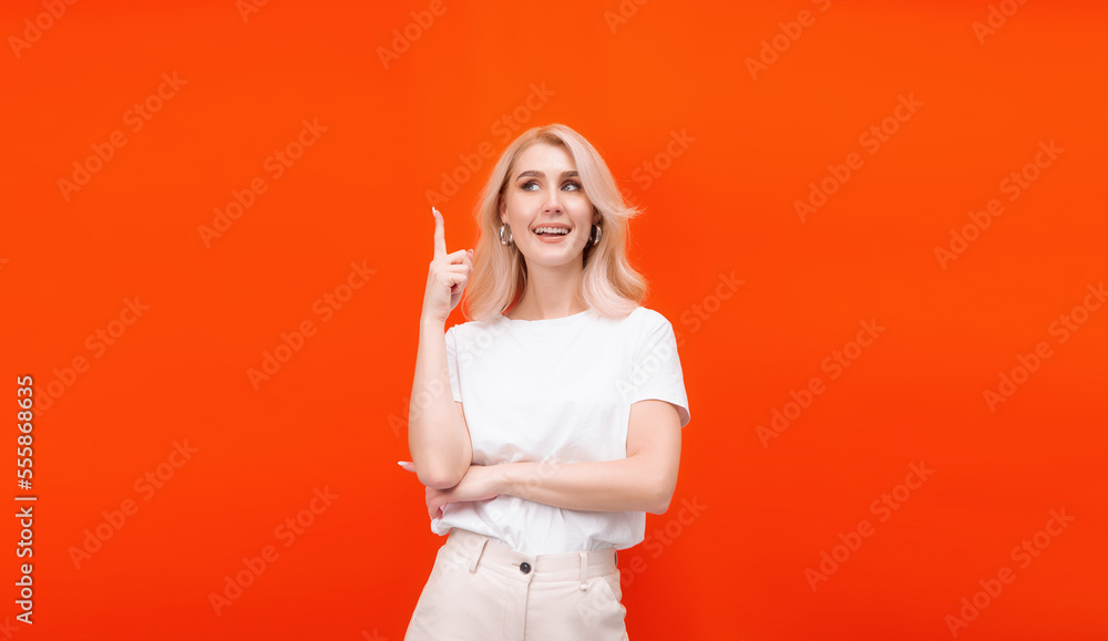 a blonde woman on an orange background in a white t-shirt stands and points with her hands with a smile a blonde woman on an orange background in a white t-shirt stands and points with her hands with a smile