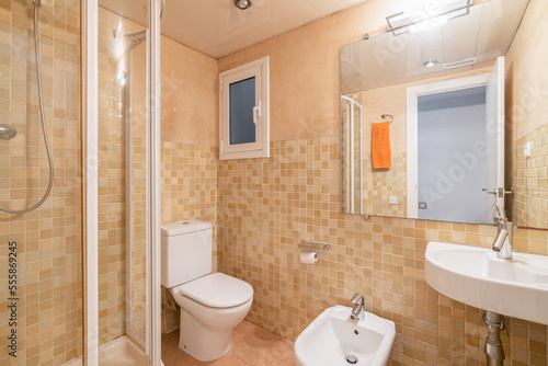 Small bathroom with toilet, shower, bidet and washbasin. Walls with ceramic tiles of beautiful orange and beige color