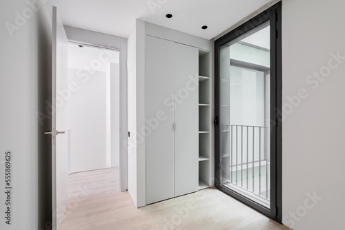 Modern style entrance hall interior  neutral white color corridor with wooden light parquet floor  sliding wardrobe and glass door in black aluminum frame with access to the street.