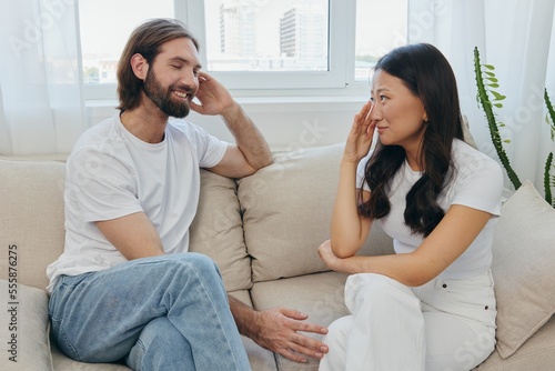 A man and a woman of different races sit on the couch in a room at home and talk about their problems to each other. A stress-free lifestyle of family quarrels with psychological support