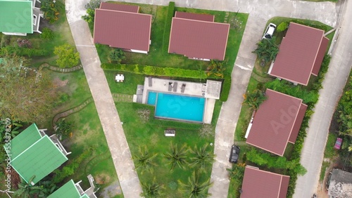 Cinematic drone shot of family vacation resort with pool in tropics and small cozy villas on the territory with a well-groomed lawn and palm trees. Rest in a hotel in the tropics during the holidays © ShantiMedia