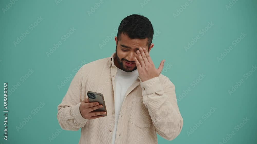 Shocked Middle Eastern young man typing on mobile in the turquoise studio Shocked Middle Eastern young man typing on mobile in the turquoise studio