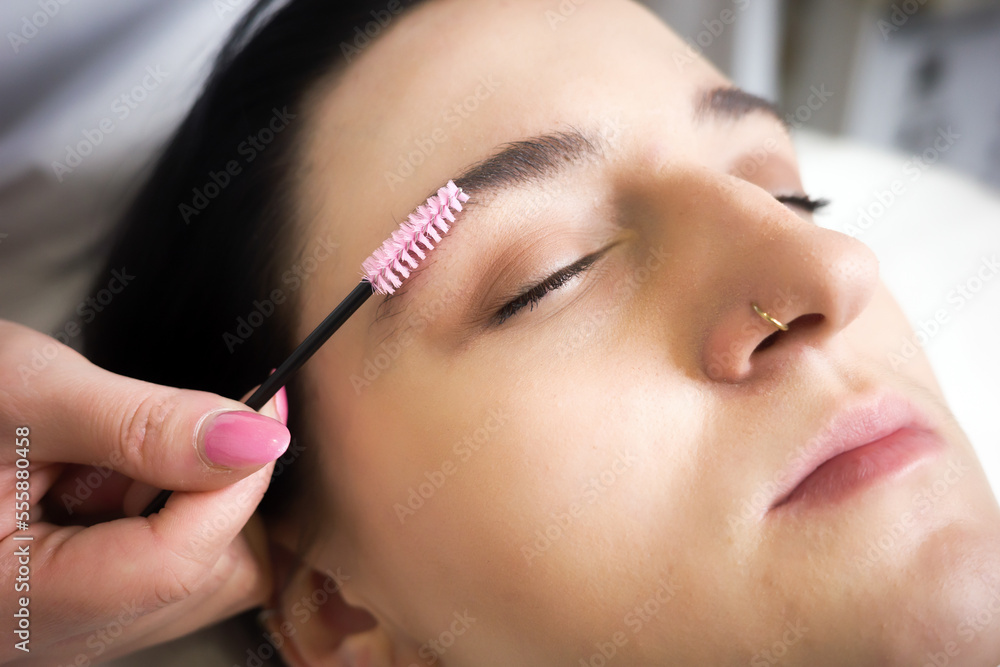 master directs the growth of hairs in eyebrows of young woman in beauty salon