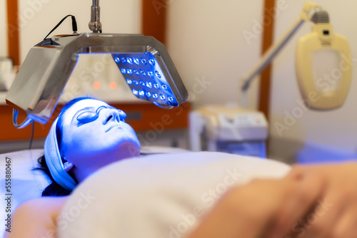 Facial treatment with led therapy. Girl on a light therapy procedure. LED lamp with blue light. Woman in protective glasses.