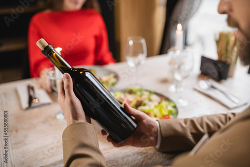 cropped view of man holding bottle with wine near girlfriend during festive dinner on valentines day