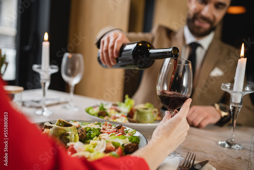 blurred man pouring red wine in glass of girlfriend during dinner on valentines day