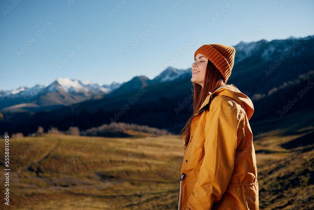 Naklejka premium Woman standing beautifully on a hill smile with teeth in the mountains in the autumn in a yellow raincoat and jeans happy sunset trip to hike the mountains in the snow, freedom lifestyle 