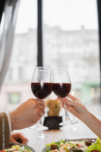 partial view of couple clinking glasses with red wine during celebration on valentines day