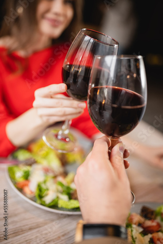 cropped view of couple clinking glasses with red wine during celebration on valentines day