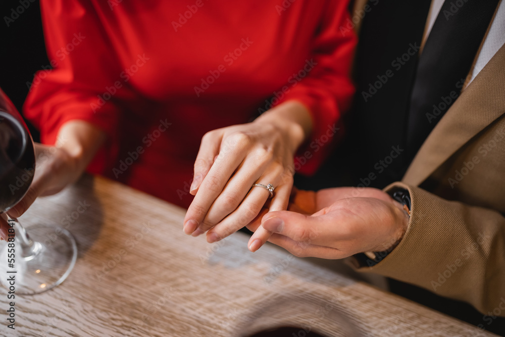 Obraz premium cropped view of man holding hand of woman with engagement ring on finger on valentines day