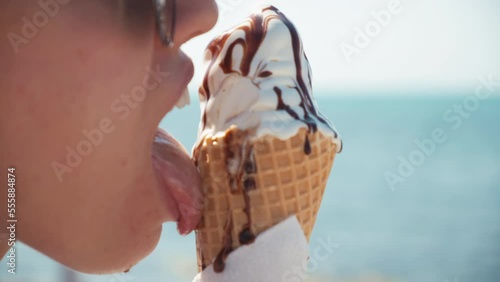a girl eats ice cream in a cone on the beach. a girl goes with an ice cream cone on the beach. close-up of lips with chocolate ice cream. hot summer. melted ice cream flows down the arm