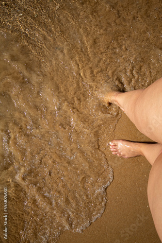 Las piernas de una mujer con curvas entrando en la orilla de la playa para bañarse en el mar en un día caluroso de primavera en la ciudad de Benidorm.