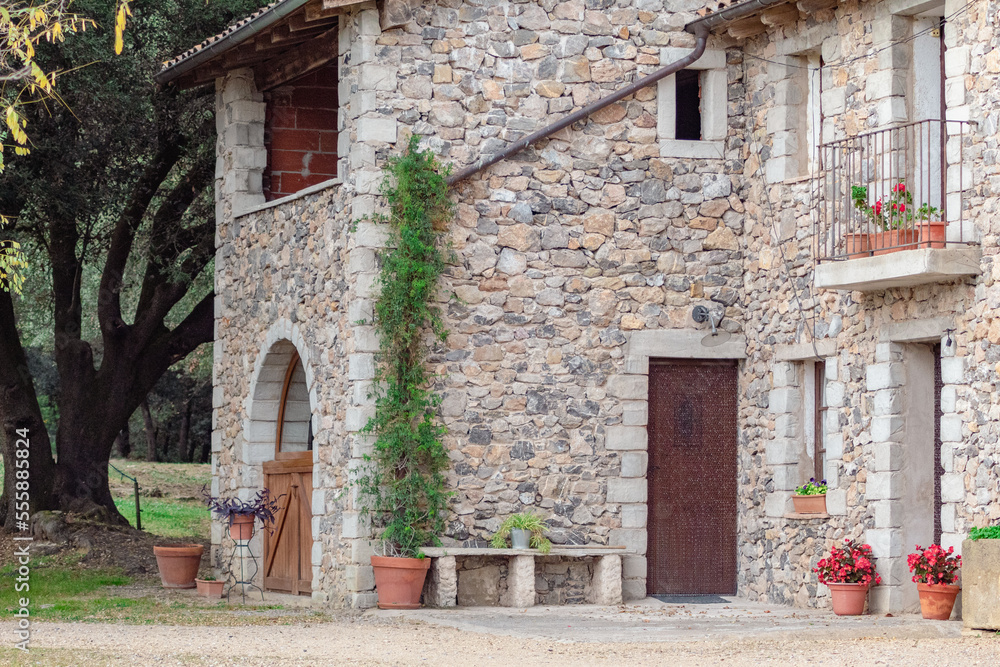 Casa de piedra con muchas flores en las puertas plantadas en maceteros de diferentes tamaños de un pequeño pueblo de Girona con las puertas de madera.