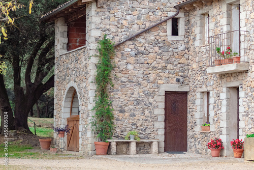 Casa de piedra con muchas flores en las puertas plantadas en maceteros de diferentes tamaños de un pequeño pueblo de Girona con las puertas de madera.