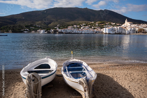 Barcas de jóvenes pescadores estacionadas en la arena de una de las playas del pueblo de cadaqués mirando hacia el tranquilo mar con la verde montaña de fondo.