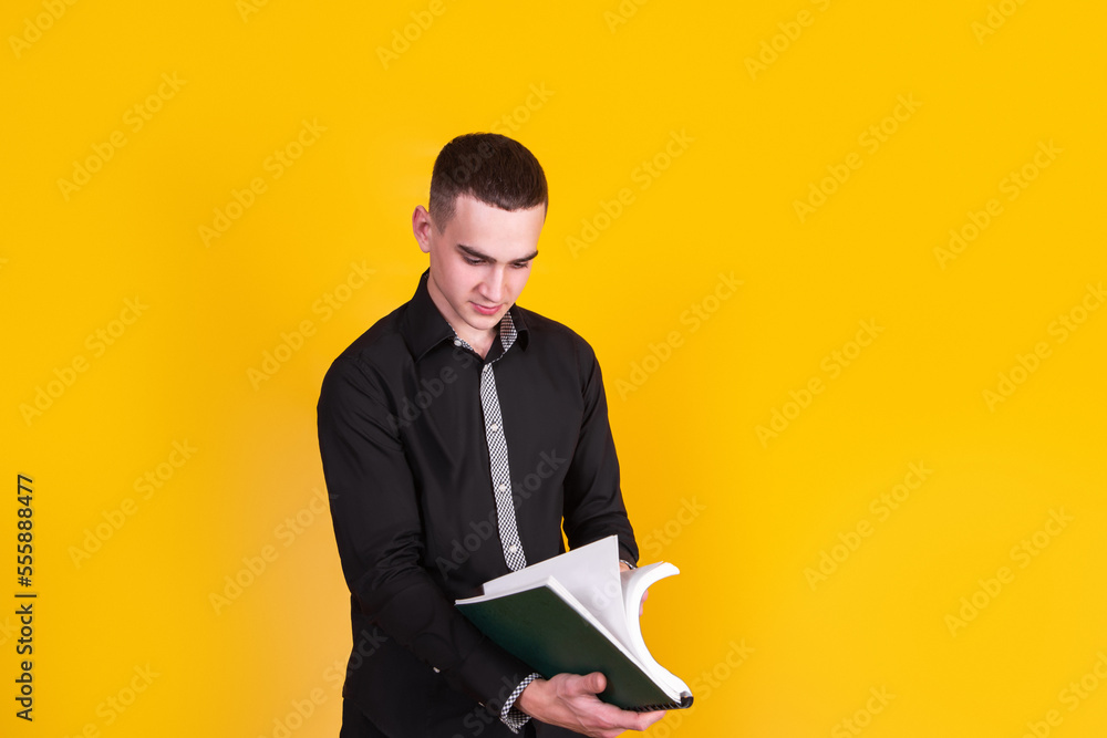 A handsome guy in a black shirt with a book on a yellow background A handsome guy in a black shirt with a book on a yellow background