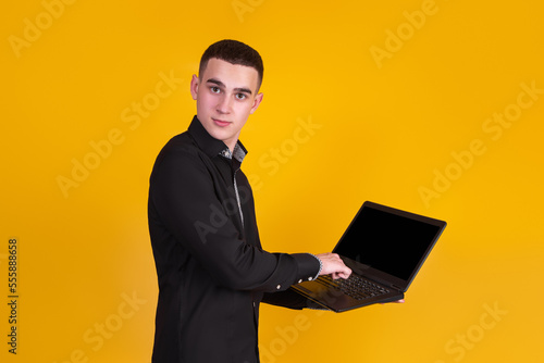 A handsome guy in a black shirt with a laptop on a yellow background