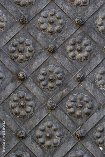 An old metal door, forged gates, rivets on the facade of a cast-iron door, a round handle to open the door, the texture of old iron.