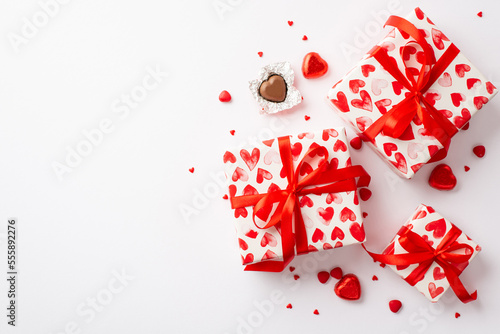 St Valentine's Day concept. Top view photo of present boxes in wrapping paper with heart pattern chocolate candies and sprinkles on isolated white background with blank space