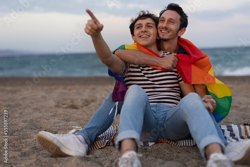 Beautiful gay young couple embraces and holds a rainbow flag. Happy couple enjoy at the beach