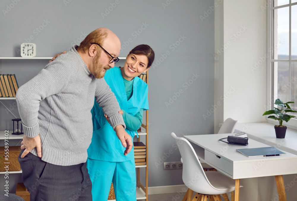 Friendly, smiling young nurse in uniform scrubs helping retired old man while walking, holding his hand, supporting him. Senior care, retirement home, assisted living facility concept