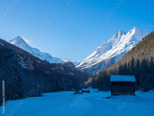 Val d'Herens, Switzerland - April 10th 2022: Winter morning view from a valley in shadow towards sunlit alpine peaks