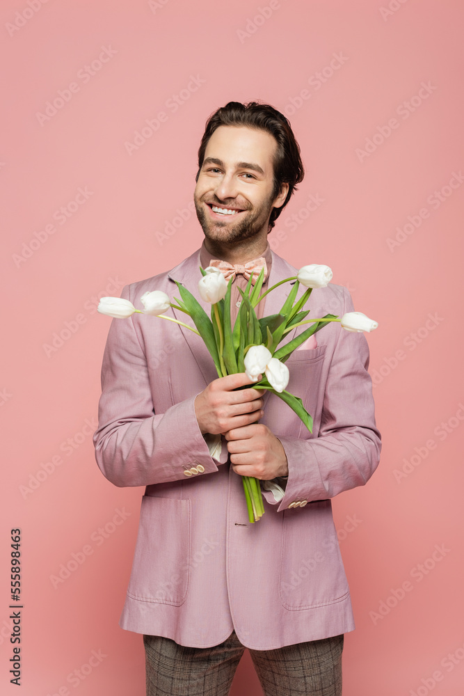 Positive host of event holding tulips and looking at camera on pink background Positive host of event holding tulips and looking at camera on pink background
