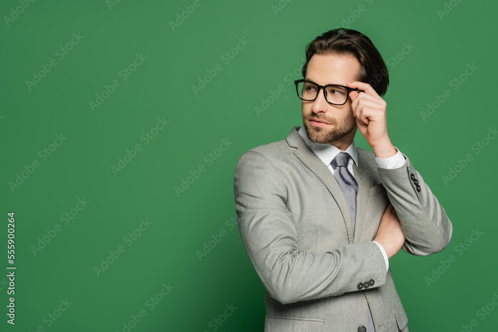 Young newscaster in suit touching eyeglasses on green background Young newscaster in suit touching eyeglasses on green background