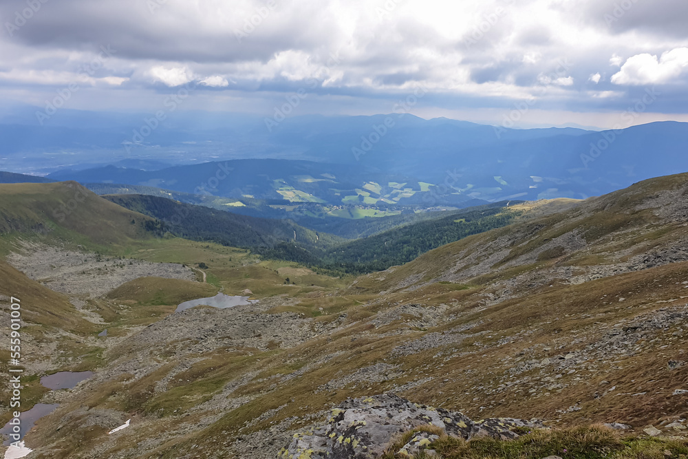 Panoramic aerial view of Lavanttal Alps and Koralpe seen from Zirbitzkogel, Seetal Alps, Styria, Austria, Europe. Landscape of hills, forest, lakes, alpine lush green pastures on a cloudy moody day