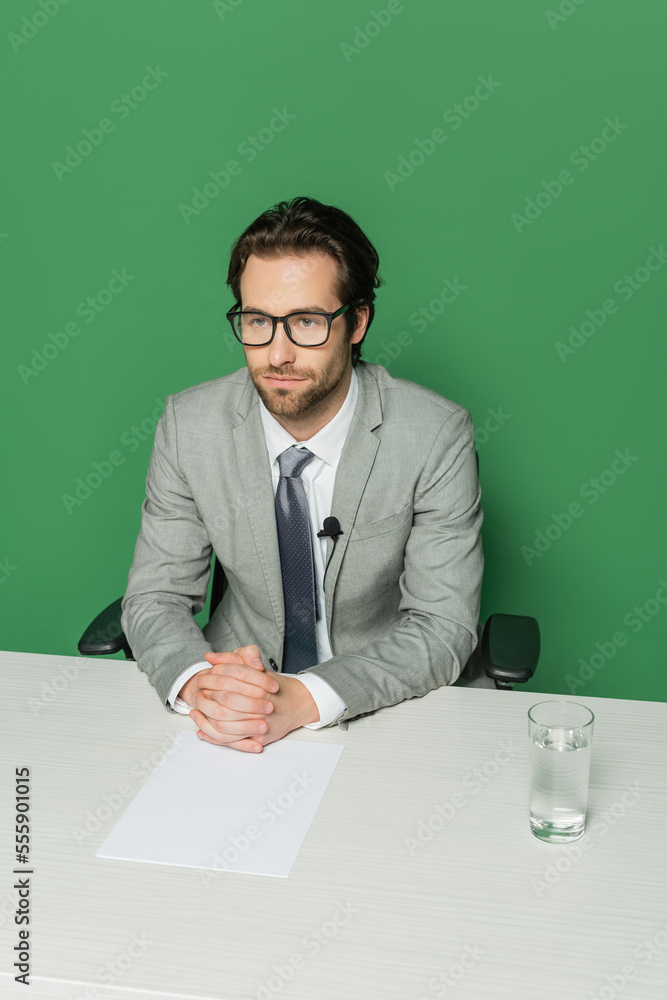 overhead view of news broadcaster in eyeglasses and suit sitting with clenched hands at desk isolated on green overhead view of news broadcaster in eyeglasses and suit sitting with clenched hands at desk isolated on green