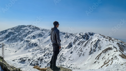 Rear view of sport man on top of summit Kreiskogel spreading arms and looking at snowcapped mountain peak Zirbitzkogel, Seetal Alps, Styria, Austria, Europe. Hiking trail Central Alps in sunny winter