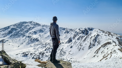 Rear view of sport man on top of summit Kreiskogel spreading arms and looking at snowcapped mountain peak Zirbitzkogel, Seetal Alps, Styria, Austria, Europe. Hiking trail Central Alps in sunny winter